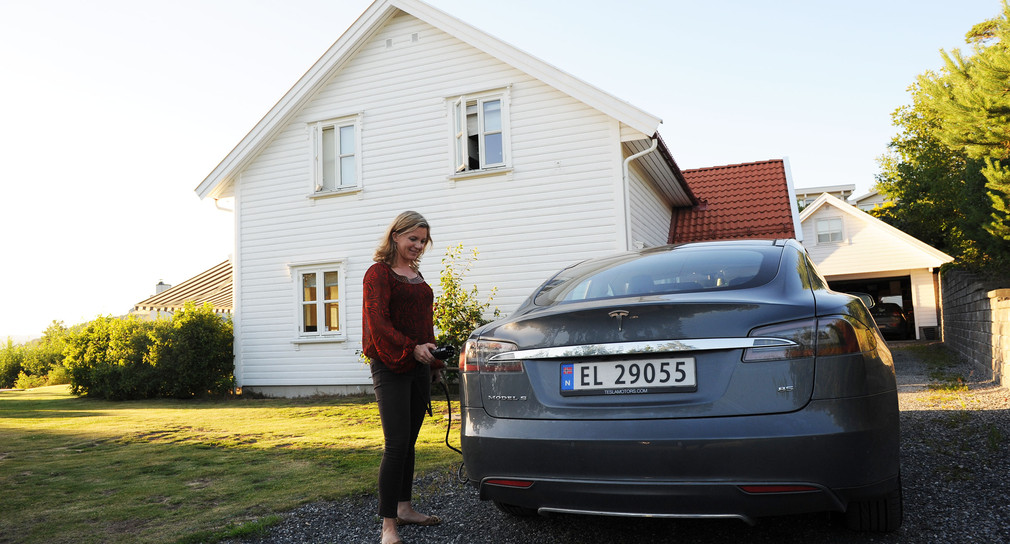 Eine Norwegerin steht vor ihrem Haus und lädt ein Elektroauto auf (Bild: © dpa).