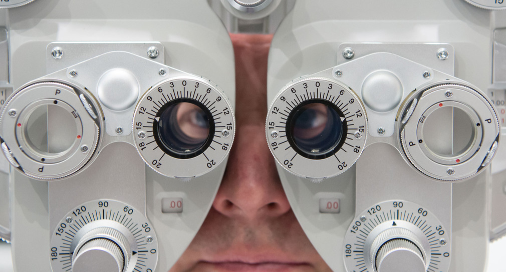 Ein Mann sitzt an einem Untersuchungsgerät mit dem ein Augenarzt die so genannte subjektive Refraktion eines Patienten bestimmen kann (Symbolbild: © dpa).