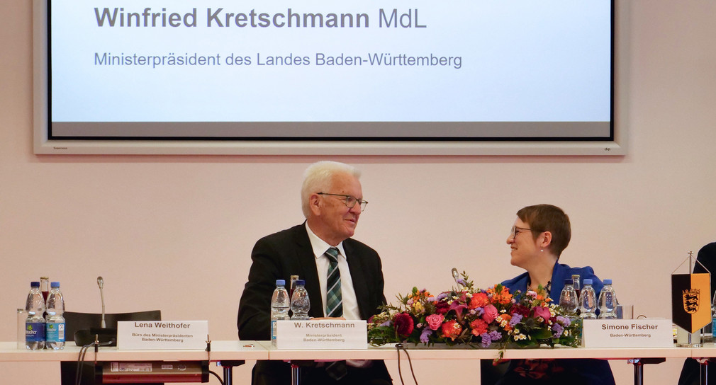 Ministerpräsident Winfried Kretschmann und Landes-Behindertenbeauftragte Simone Fischer im Gespräch an Konferenztisch.