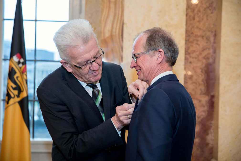 Ministerpräsident Winfried Kretschmann (l.) heftet Rainer Reichhold (r.) das Bundesverdienstkreuz ans Revers