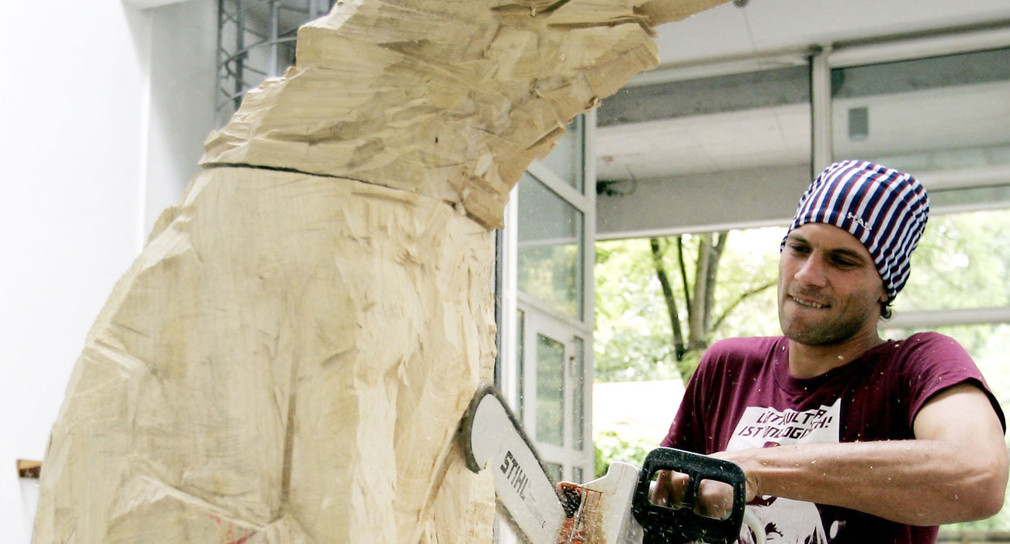 Ein Bildhauer arbeitet in einem Atelier an einer Holzskulptur. (Foto: © dpa)