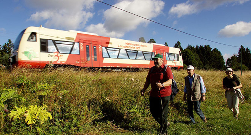 Ein Zug der Hohenzollerischen Landesbahn (HzL) fährt an einer Gruppe Wanderer vorbei (Bild: © Ralf Graner).