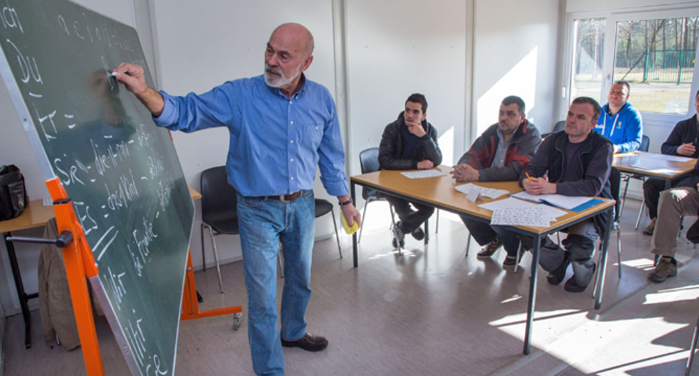 Ein Lehrer schreibt vor Asylbewerbern deutsche Vokabeln an eine Schultafel. (Foto: © dpa)