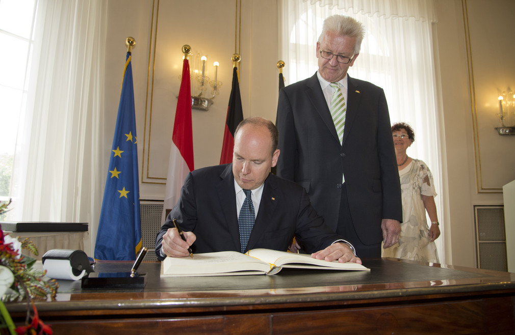Fürst Albert II. von Monaco (l.) trägt sich in das Gästebuch der Landesregierung ein; rechts dahinter steht Ministerpräsident Winfried Kretschmann