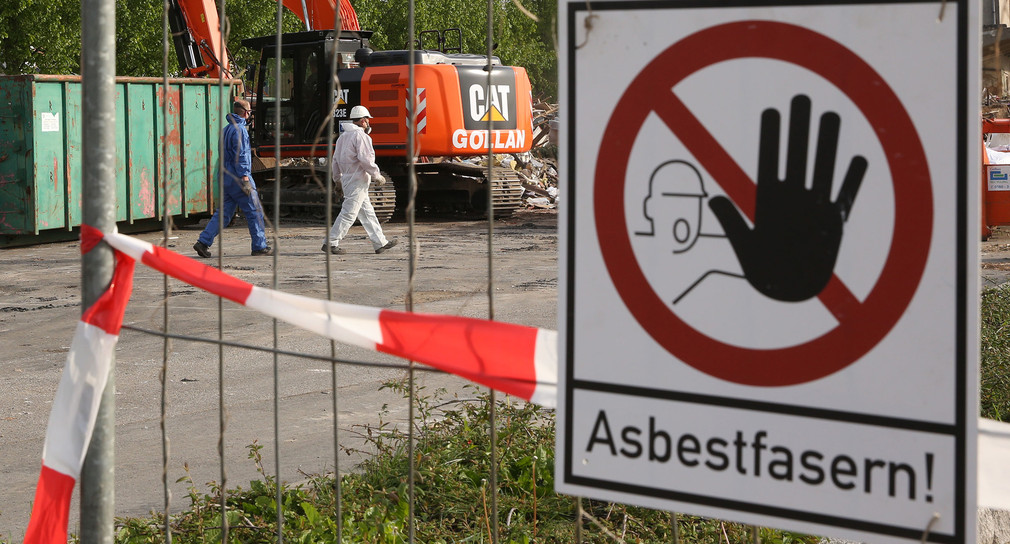 Auf einem Sammelplatz, auf dem asbestbelasteter Schutt lagert, warnt ein Schild: „Asbestfasern!“. (Foto: © dpa)