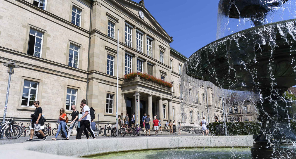 Studentinnen und Studenten laufen vor der Neuen Aula der Universität Tübingen an einem Brunnen vorbei.