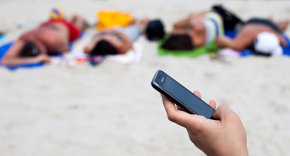 Eine Frau hält ein Mobiltelefon am Ostseestrand von Kolberg, Polen (Quelle: © dpa).