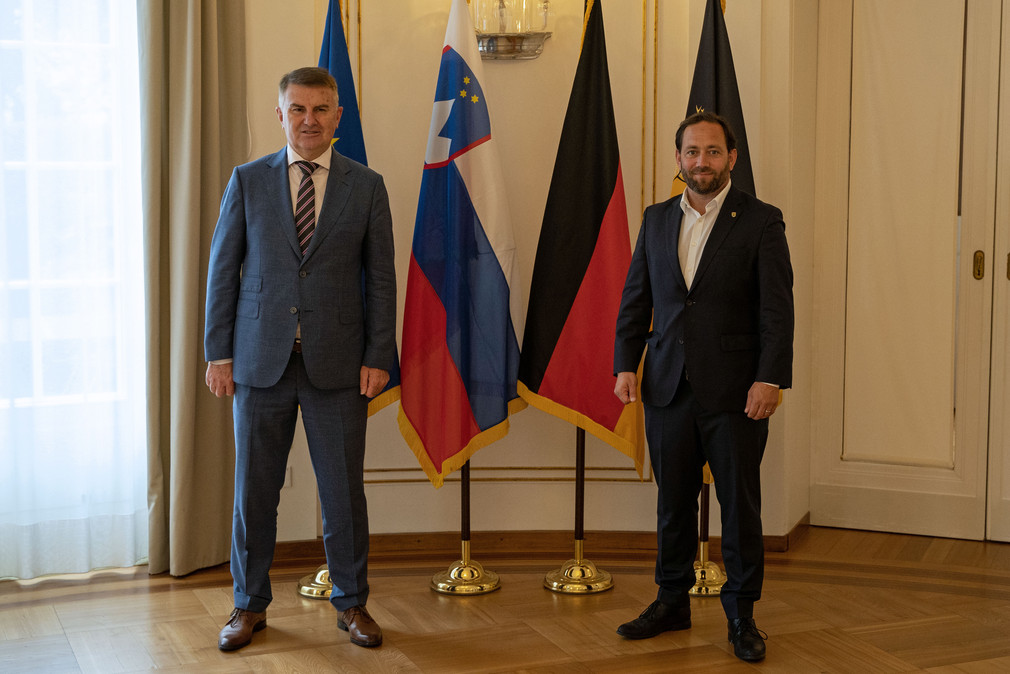 Staatssekretär Florian Hassler (r.) und der slowenische Botschafter Franc But (l.) stehen vor Fahnen.