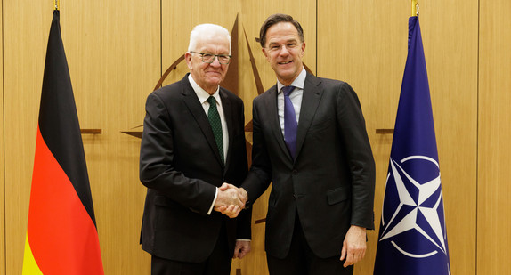 Ministerpräsident Winfried Kretschmann (links) und NATO-Generalsekretär Mark Rutte (rechts) stehen zwischen Fahnen und geben sich die Hand.