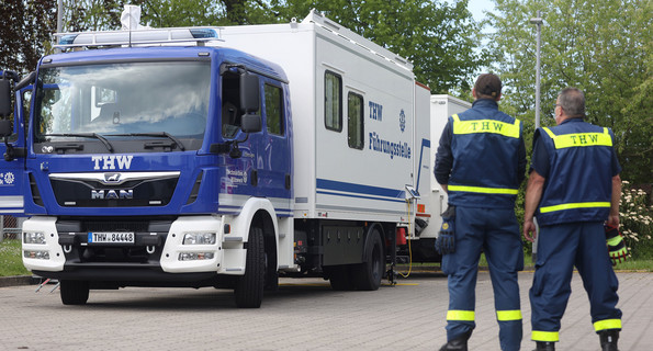 Zwei Mitarbeitende des THW stehen vor einem THW-Einsatzfahrzeug.