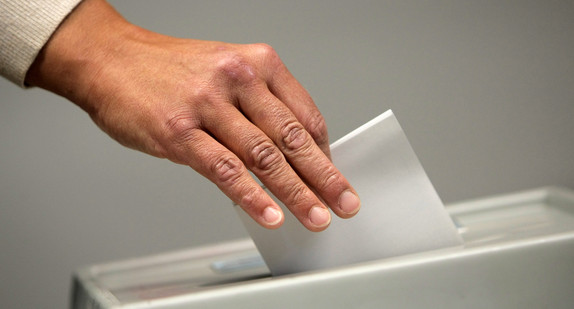 Eine Frau wirft bei einer Wahl einen Stimmzettel in eine Urne.