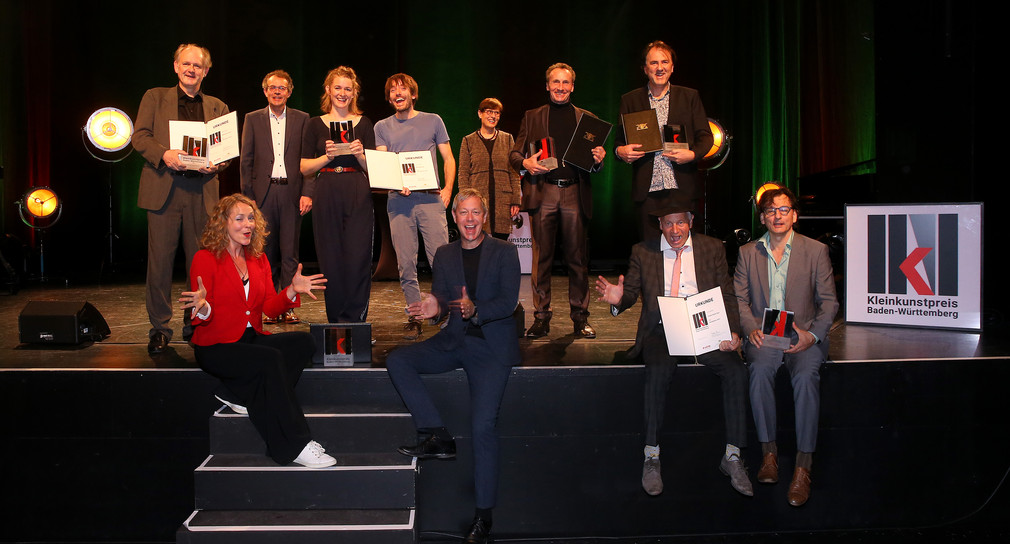 Die Preisträger des Kleinkunstpreises Baden-Württemberg 2021 stehen und sitzen auf einer Bühne.