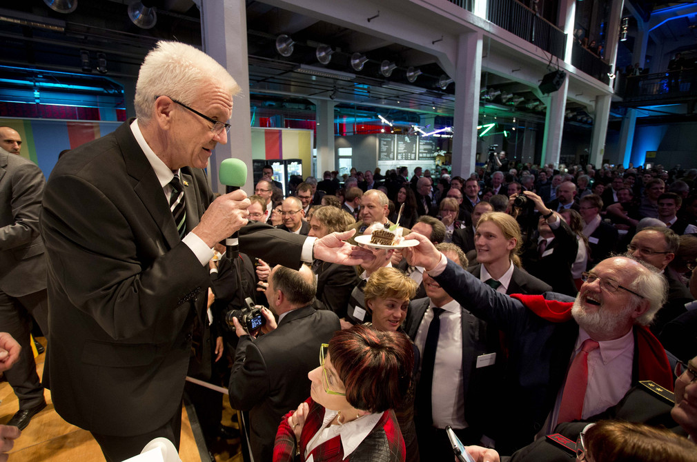 Ministerpräsident Winfried Kretschmann (l.) reicht einem Gast ein Stück Torte