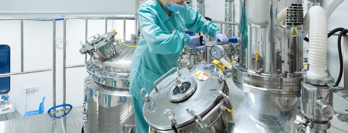 Auf dem Bild ist eine Person in Schutzkleidung zu sehen, die an einem chemischen Reaktor in einem Reinraum arbeitet.
