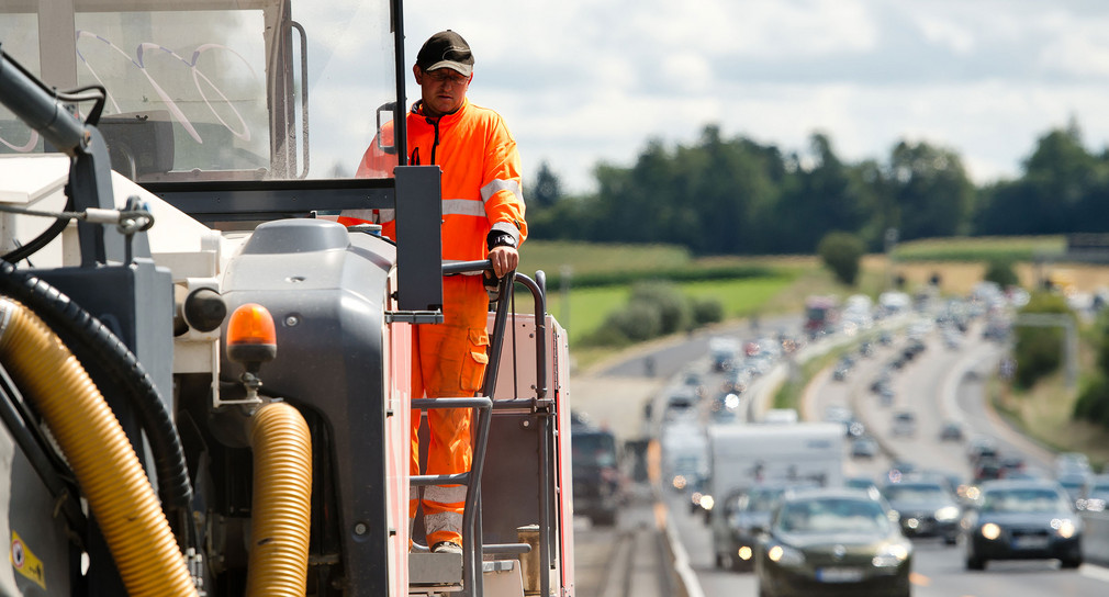 Ein Bauarbeiter bedient eine große Baumaschine auf einer Autobahnbaustelle. (Bild: © dpa)