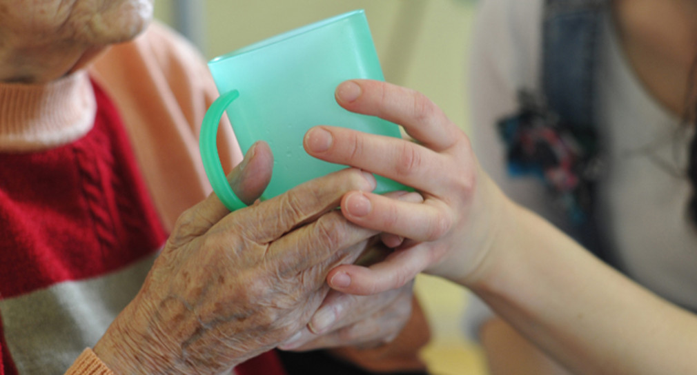 Eine Pflegekraft hilft einer alten Frau beim Trinken aus einem Becher in einem Seniorenheim. (Bild: © dpa)