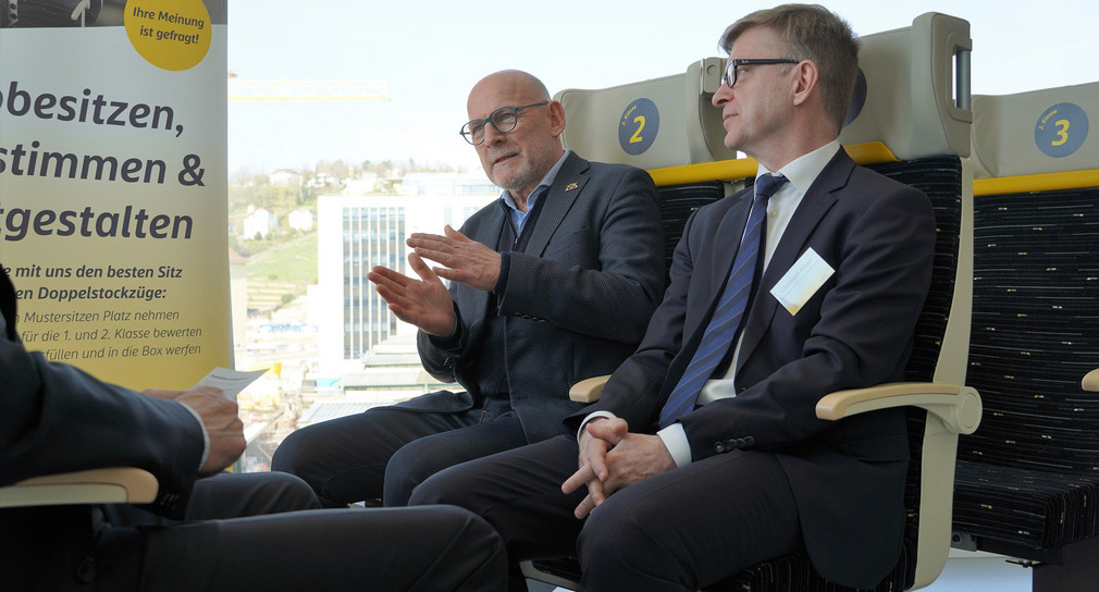 Verkehrsminister Winfried Hermann (rechts hinten) und Christoph Klaes, Vertriebsleiter beim Fahrzeughersteller Alstom (rechts vorne) testen Sitze der neuen Doppelstockzüge.