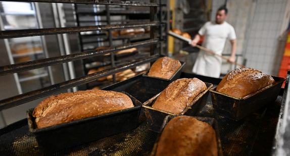 Bäcker in einer Backstube holt Brote aus dem Ofen.