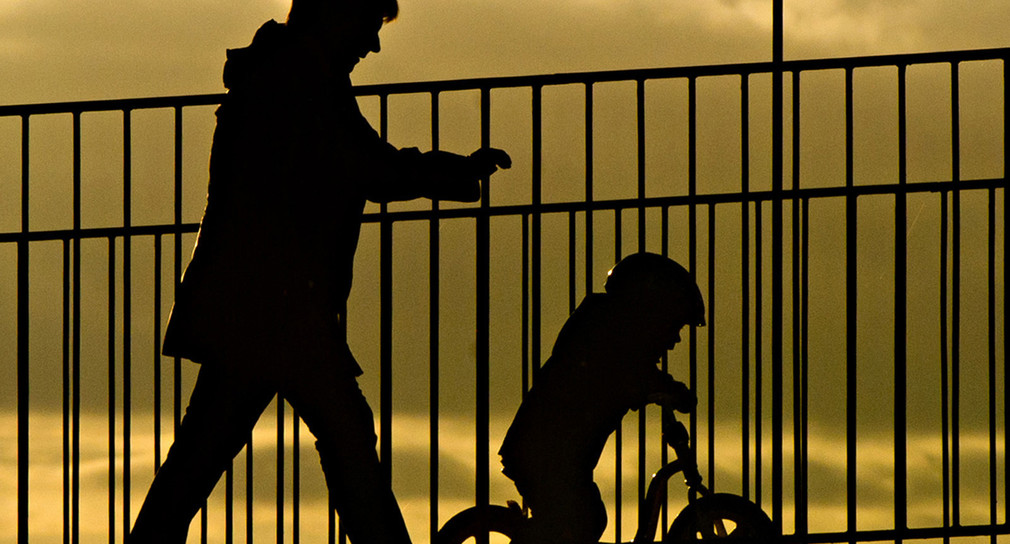 Eine Frau geht mit einem Kind bei Sonnenaufgang in Stuttgart über eine Brücke. (Bild: dpa)
