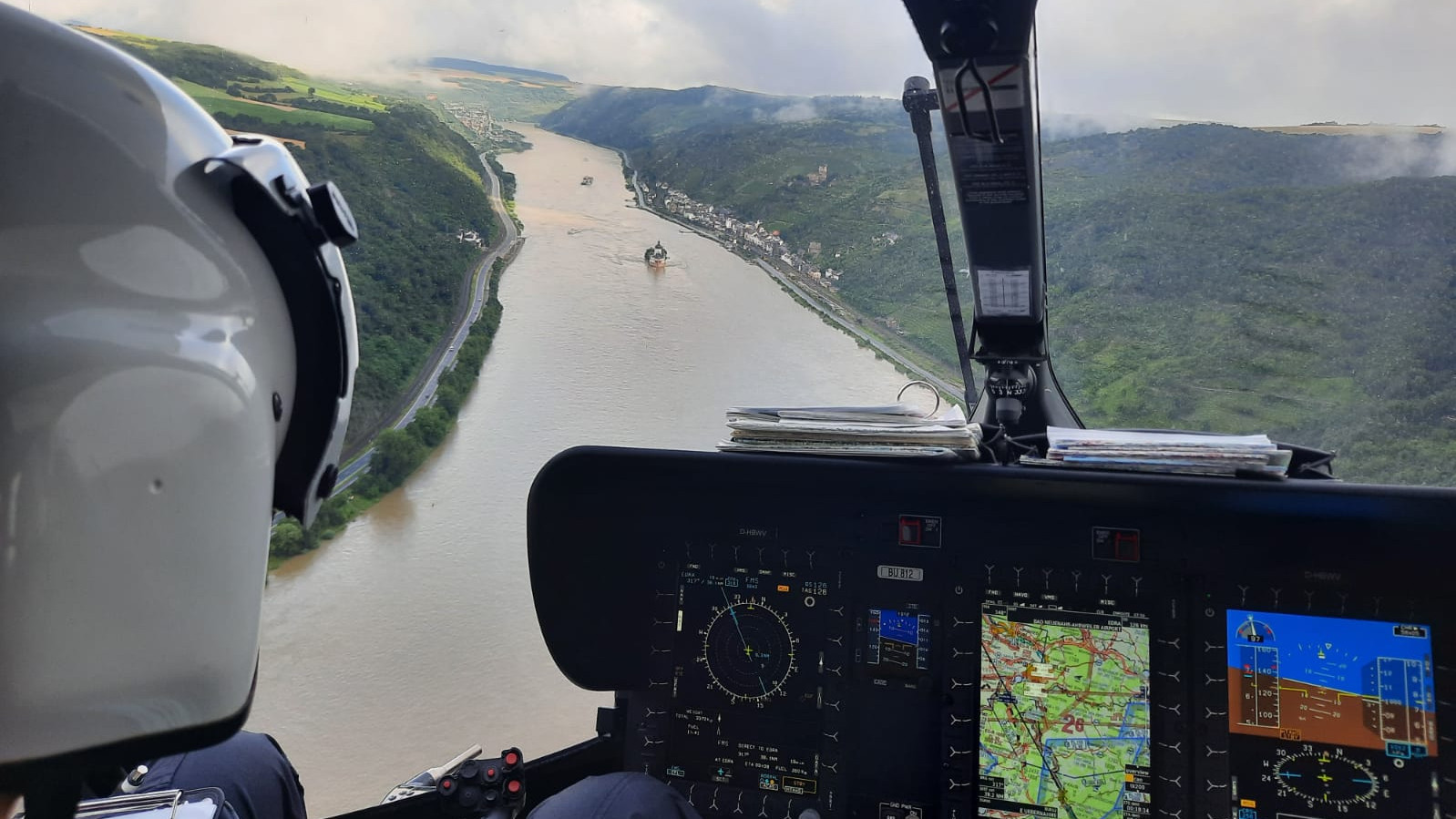 Blick aus dem Cockpit eines Hubschraubers auf einen überschwemmten Fluss.']