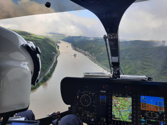 Blick aus dem Cockpit eines Hubschraubers auf einen überschwemmten Fluss.']