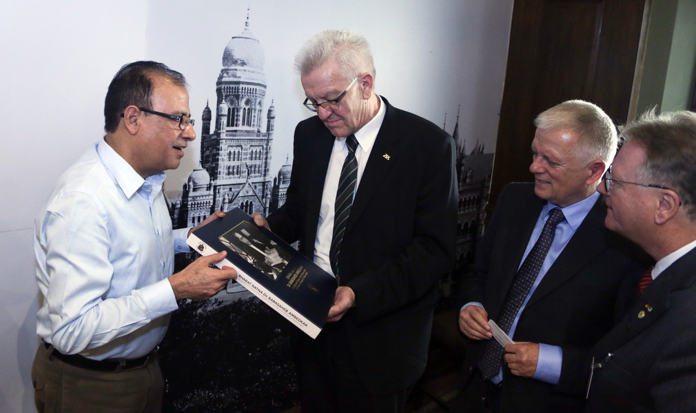 Der Verwaltungsdirektor der Stadt Mumbai, Municipal Commissioner Ajoy Mehta (l.), übergibt Ministerpräsident Winfried Kretschmann (M.) ein Buch.
