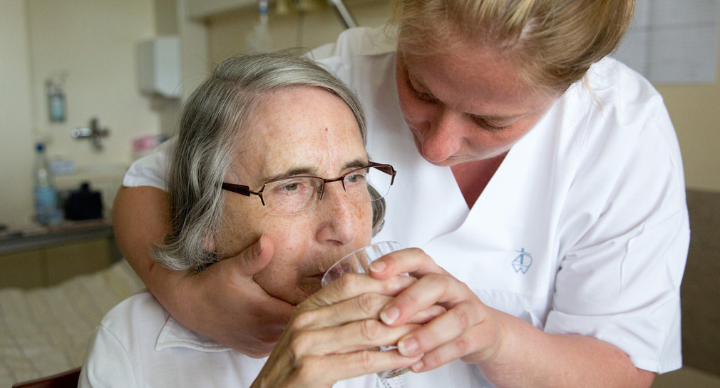 Eine Pflegerin hilft einer älteren Frau beim Trinken. (Foto: dpa)