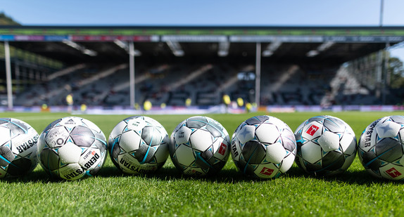 Fußbälle liegen vor der Tribüne auf dem Rasen.