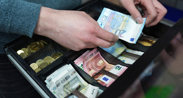 Hände eines Kioskmitarbeiters legen Geld in eine Kasse.
