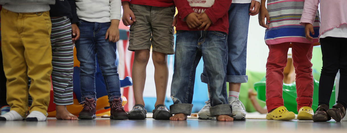 Mehrere Kinder stehen nebeneinander in einem Kindergarten. (Bild: © Christian Charisius/dpa)