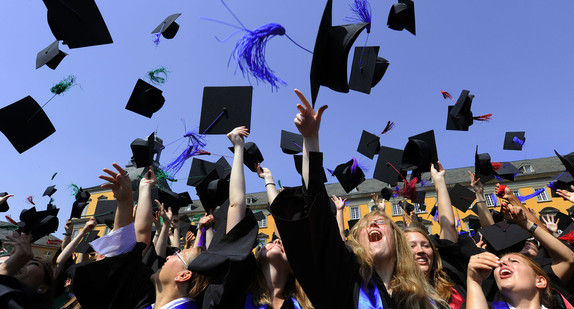 Universitäts-Absolventen werfen auf dem Campus in Talare gekleidet ihre Barette in die Luft (Symbolbild: © dpa).