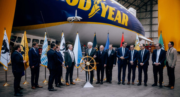 Die IBK-Regierungschefs bei der symbolischen Steuerradübergabe im Zeppelin-Hangar Friedrichshafen, im Hintergrund steht ein Zeppelin.