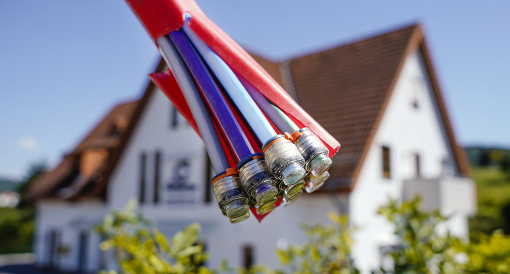 Ein Bündel mit Umhüllungen für Glasfaserkabel hängt vor einem Haus in Oberflockenbach. (Bild: picture alliance/Uwe Anspach/dpa)