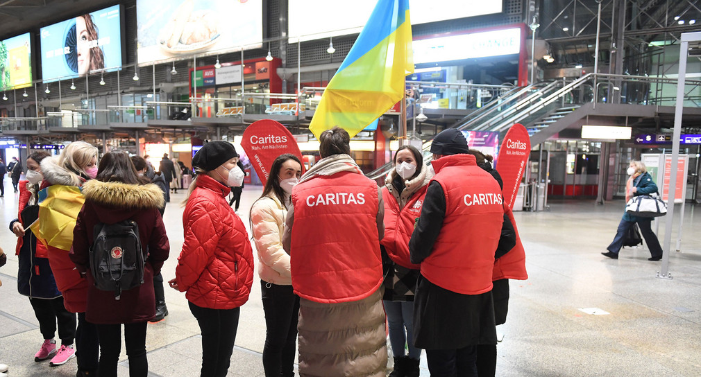 Mitarbeitende der Caritas stehen am Münchner Hauptbahnhof um Frauen und Männer aus der Ukraine zu empfangen.