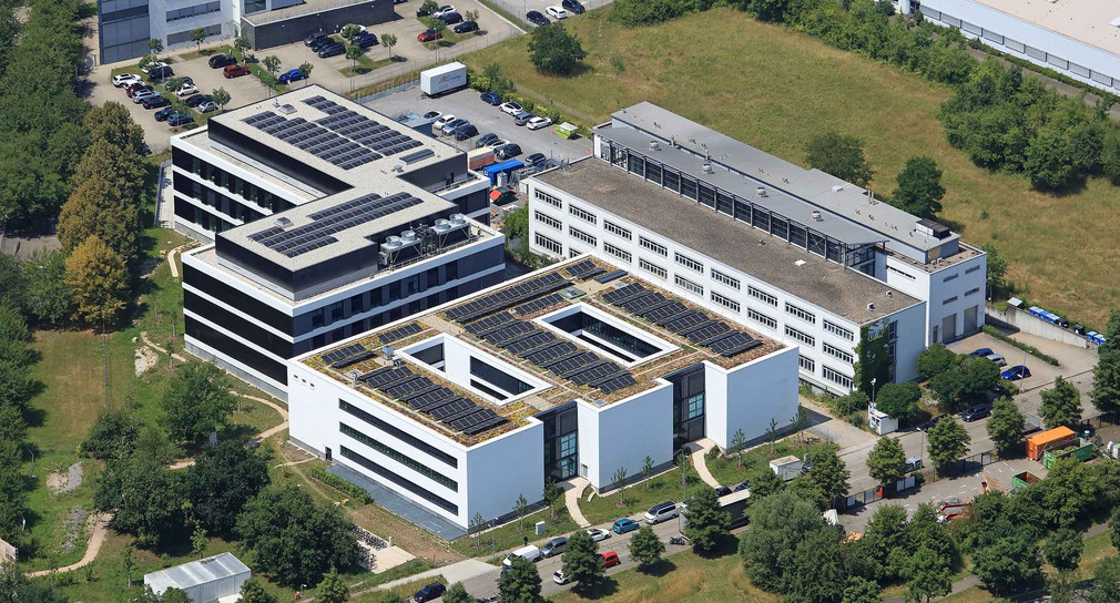 Luftaufnahme des neuen Büro- und Laborgebäudes der Landesanstalt für Umwelt Baden-Württemberg (LUBW) in Karlsruhe mit begrünten Dachflächen und Photovoltaikanlagen, umgeben von weiteren Bürogebäuden und Grünflächen.