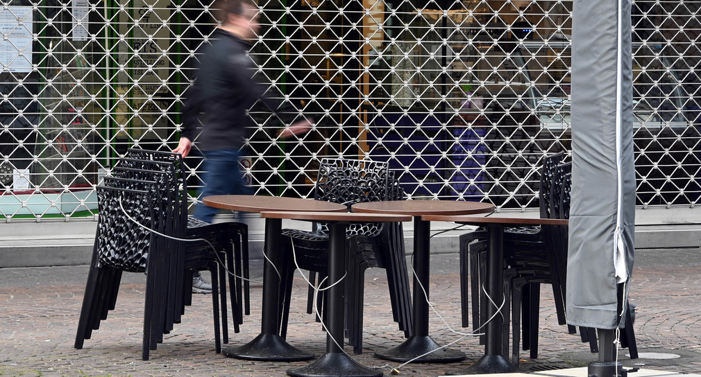 Ein Passant geht in der Karlsruher Fußgängerzone an einem geschlossenen Geschäft und den gestapelten Stühlen eines Straßencafés vorbei. (Bild: picture alliance/Uli Deck/dpa)
