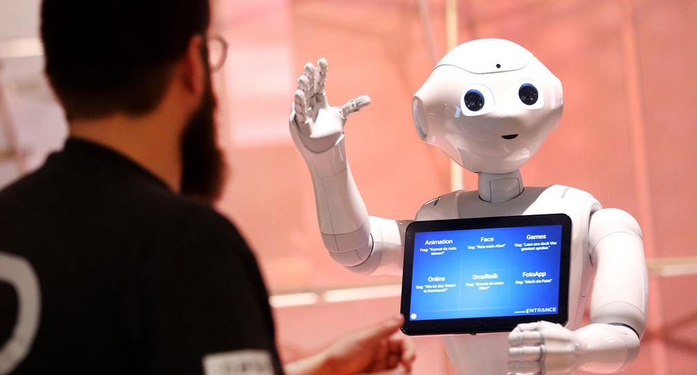 Ein humanoider Roboter kommuniziert im Rahmen einer Ausstellung zu künstlicher Intelligenz  mit einem Besucher.