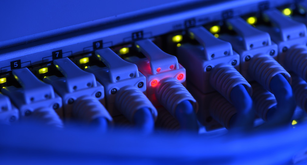 Ein Netzwerk-Kabelstecker leuchtet in der Netzwerkzentrale einer Firma zu Kontrollzwecken rot. (Bild: picture alliance/Felix Kästle/dpa)