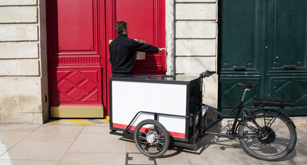 Ein Paketzusteller liefert ein Paket mit einem elektrischen Lastenrad.