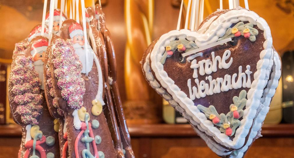 Ein Lebkuchenherz mit der Aufschrift „Frohe Weihnacht“ hängt auf einem Weihnachtsmarkt (Bild: © dpa).