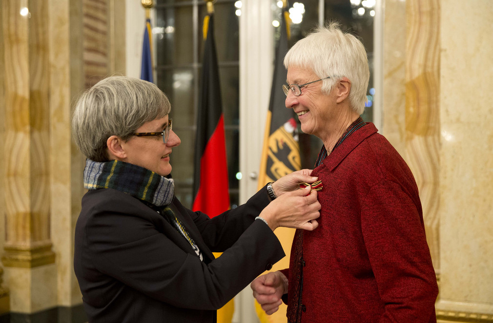 Ministerin Silke Krebs (l.) steckt Ursula Marx (r.) das Bundesverdienstkreuz an.