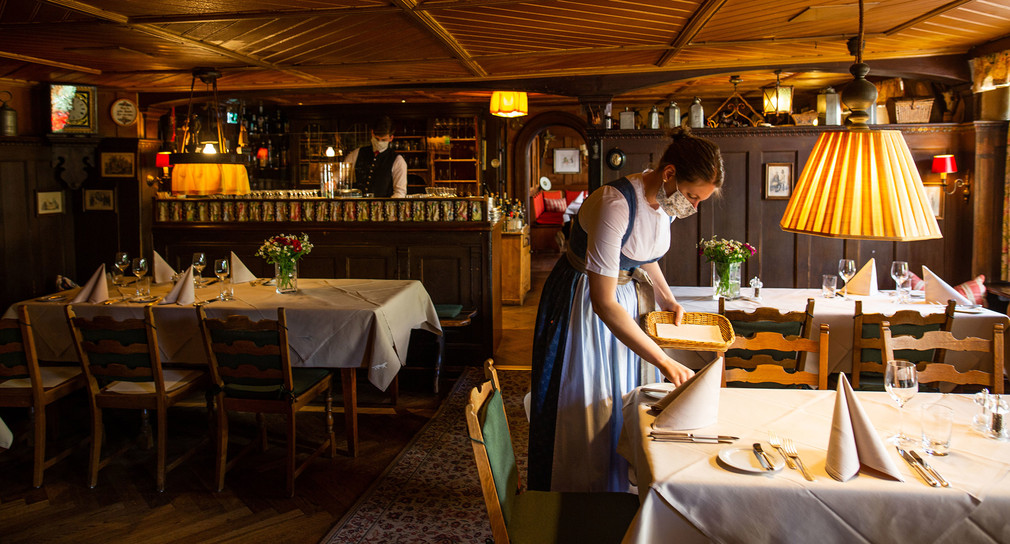 Eine Frau deckt in einem Restaurant in Münstertal einen Tisch ein und trägt Mundschutz.