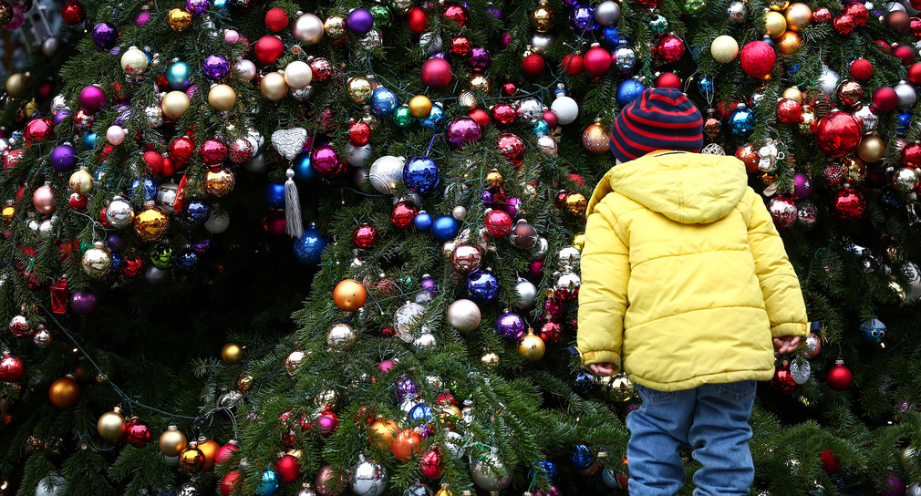 Symbolbild: Ein Kind betrachtet einen mit Christbaumkugeln behangenen Weihnachtsbaum. (Bild: dpa)