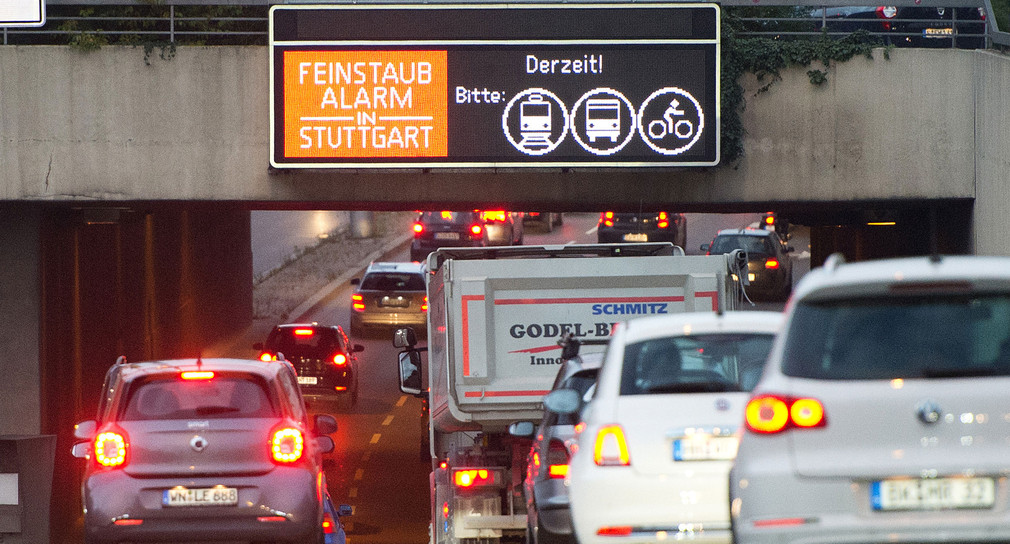 Autos fahren in der Innenstadt von Stuttgart an einem Hinweisschild mit der Aufschrift „Feinstaubalarm“ vorbei (Bild: © dpa).