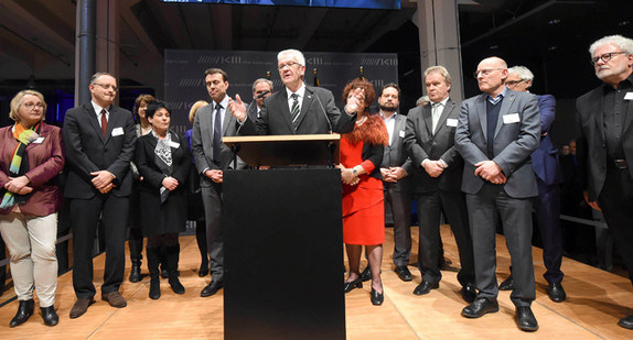 Ministerpräsident Winfried Kretschmann (M.) bei seiner Ansprache, rechts und links neben ihm stehen die Kabinettsmitglieder (Foto: dpa)