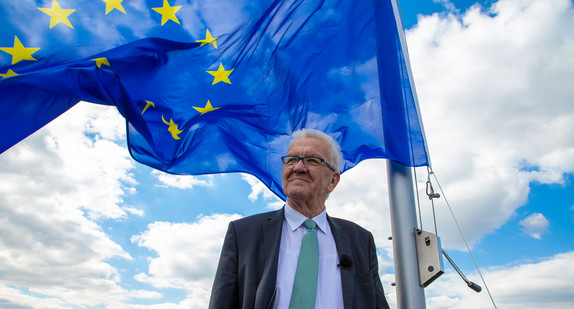 Ministerpräsident Winfried Kretschmann steht vor der auf dem Dach der Villa Reitzenstein gehissten Europafahne.