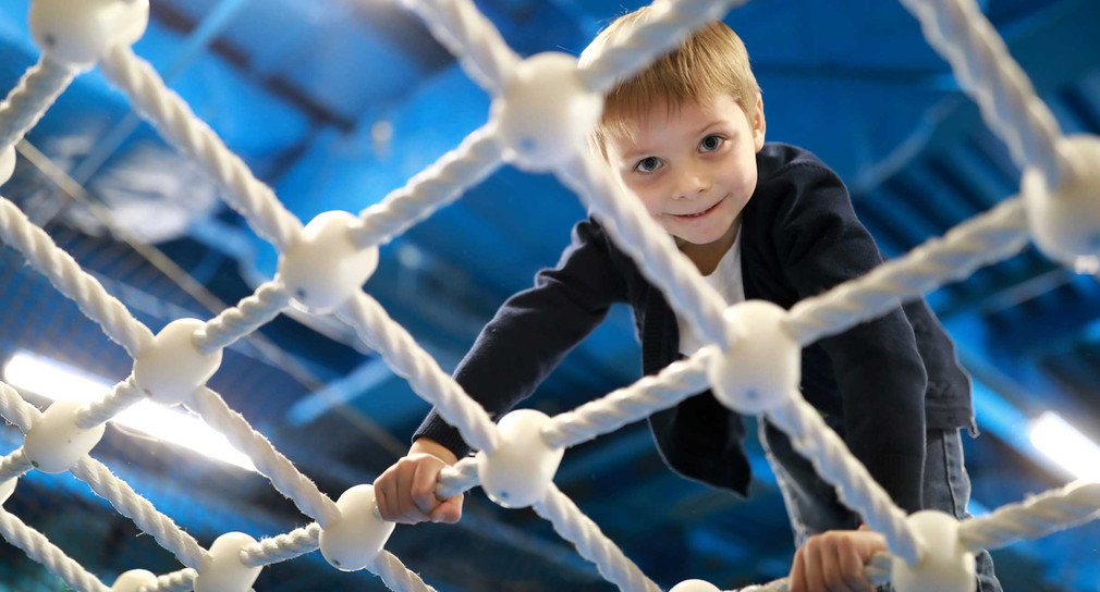 Ein Junge klettert auf einem Indoor-Spielplatz über ein Kletternetz.