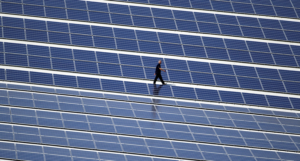 Ein Techniker läuft über ein Dach, auf dem eine Photovoltaik-Anlage montiert wurde. (Bild: © picture alliance/Jens Büttner/dpa-Zentralbild/dpa)