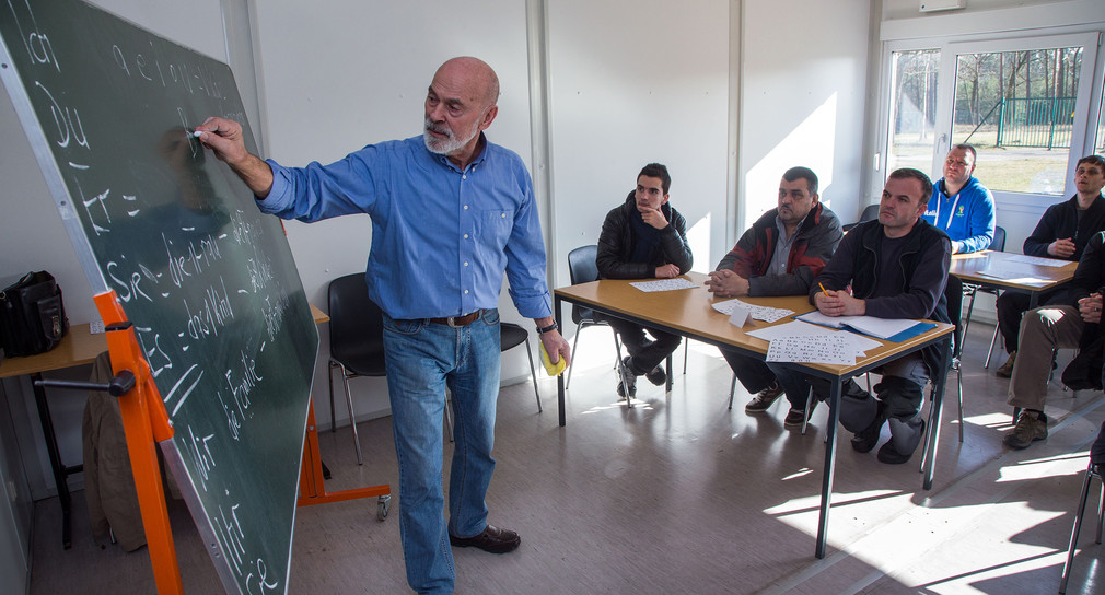 Ein Lehrer schreibt vor Asylbewerbern deutsche Vokabeln an eine Schultafel. (Foto: Jens Büttner/dpa)