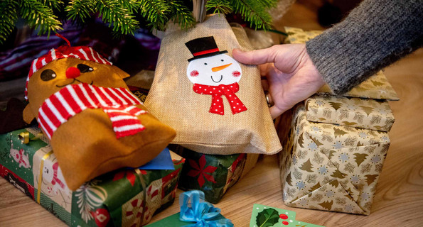 Eine junge Frau legt an Heiligabend mehrere Geschenke unter einen Weihnachtsbaum.